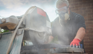 A man wearing a respirator while cutting a piece of stone block, to ensure proper silica dust protection