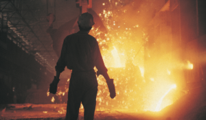 A worker silhouetted against molten metal which is being poured out in front of him