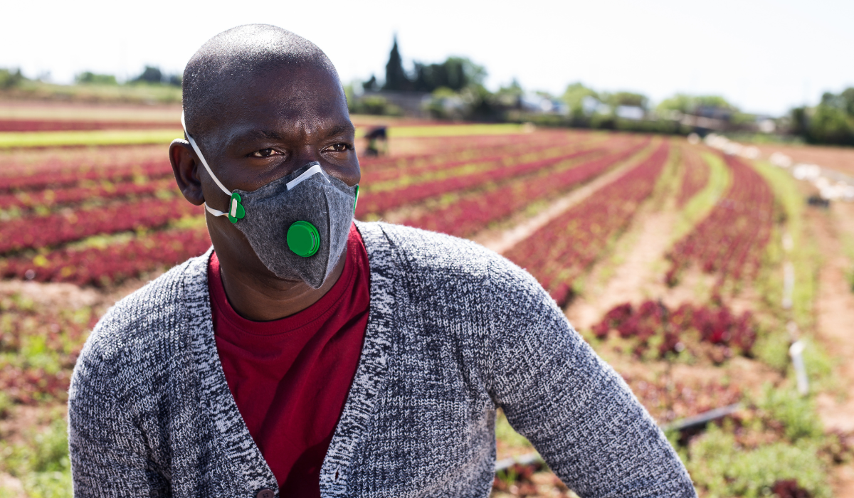 A farm employee standing in a field, wearing a protective mask, highlighting the need for respiratory protection for farm workers