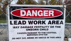 A"Danger" sign posted on a fence, listing the dangers of lead exposure and warning that the work area contains lead.