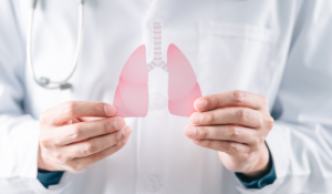A close up of a doctor in a white coat holding up what appears to be a paper cutout or computer-generated image of a set of lungs. Respiratory health challenges worksite medical