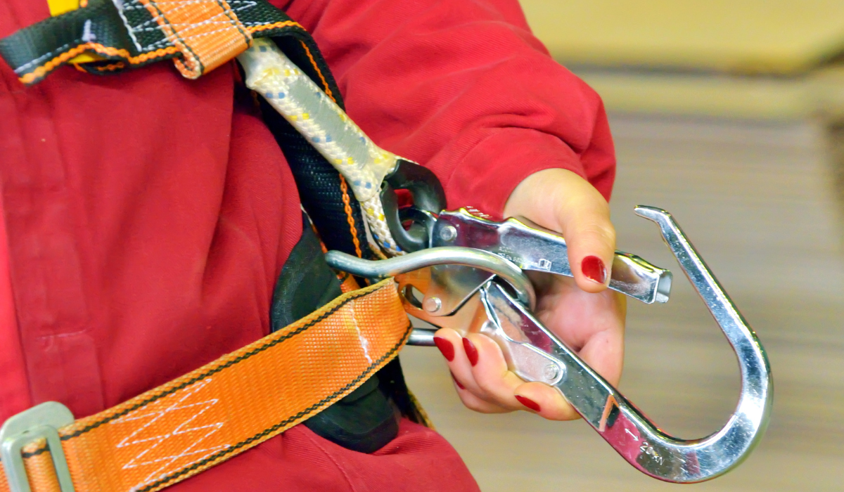 A closeup of a worker who is holding their safety harness hookup attachment in their hand, showing their ppe for fall prevention