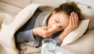 A sick woman lying down blowing her nose, wishing she had utilized seasonal flu prevention strategies
