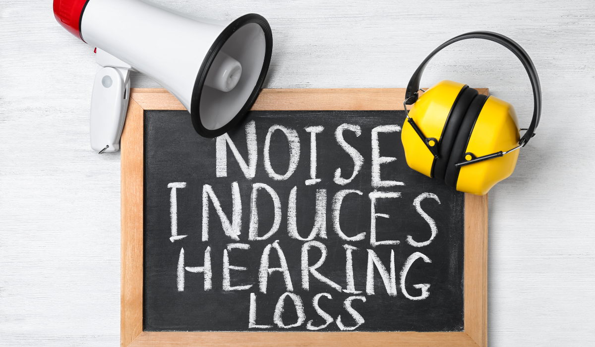 A small chalkboard laying flat on a table, along with a megaphone and a pair of earmuffs. the chalkboard reads: Noise induces hearing loss