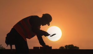 A construction worker silhouetted against the summer sun, laying cement, at risk of heat illness if not careful