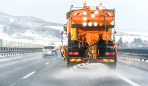 A salt truck driving down the road, spreading salt or other chemical deicers on the road.