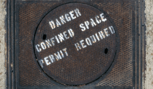 An image of a sewer manhole cover. Spray painted across the cover are the words "Danger Confined Space, Permit Required